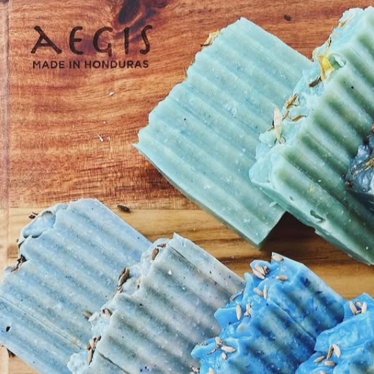 Blue and green soap bars with visible herbs on a wooden surface, branded &