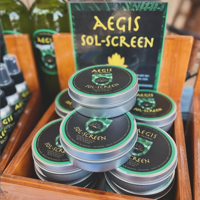 Stack of Aegis Sol-Screen tins in a wooden box with promotional materials in the background.