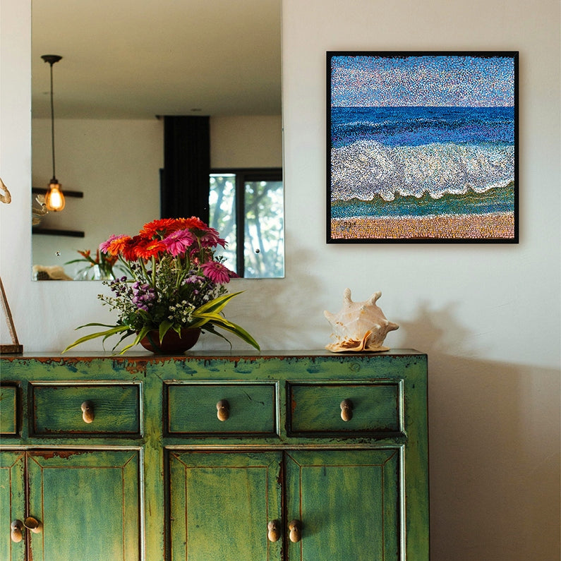 Green distressed cabinet with a mirror, flowers, and a painting on a wall.