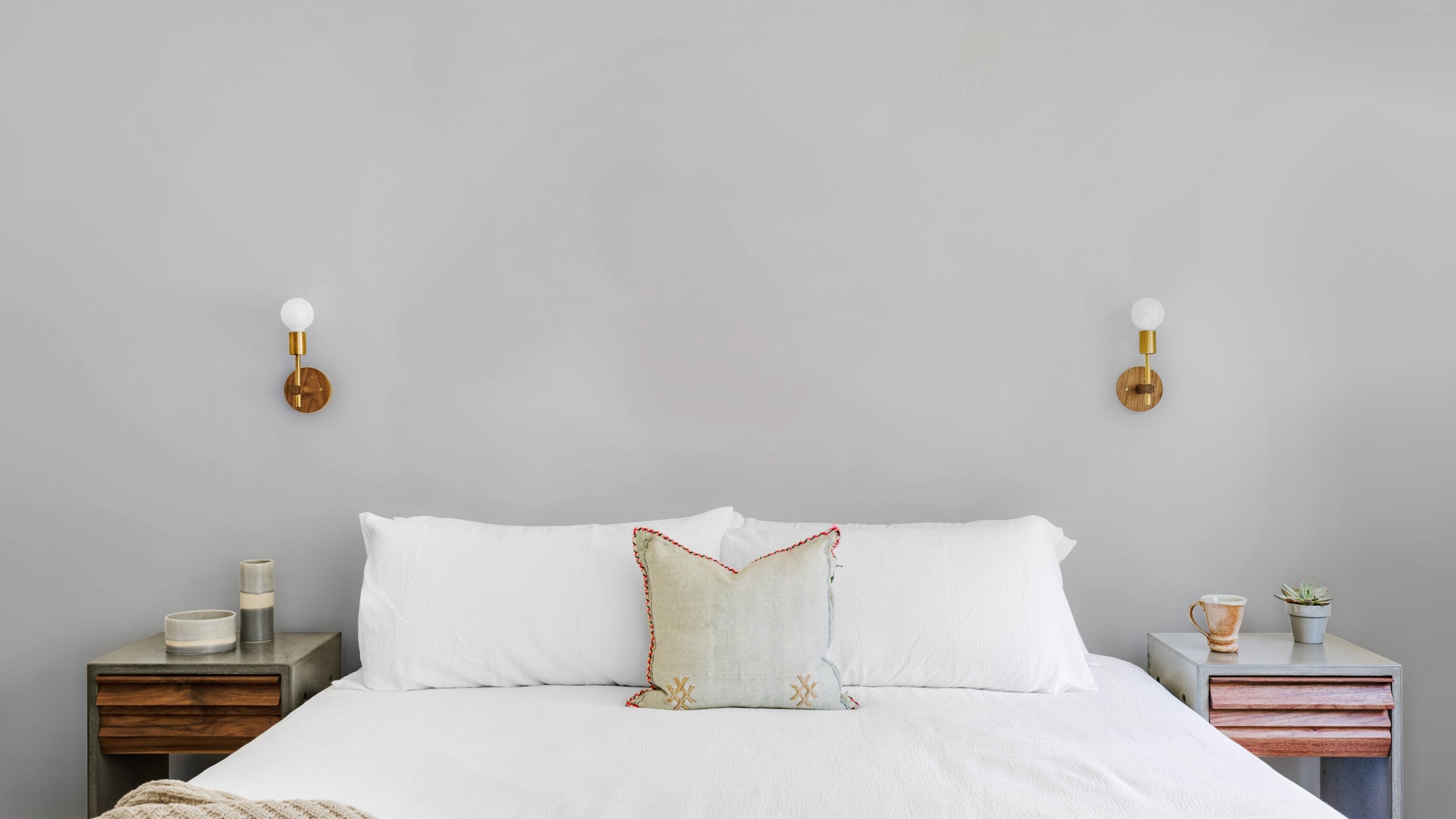 Bedroom with a neatly made bed, nightstands, and wall sconces.