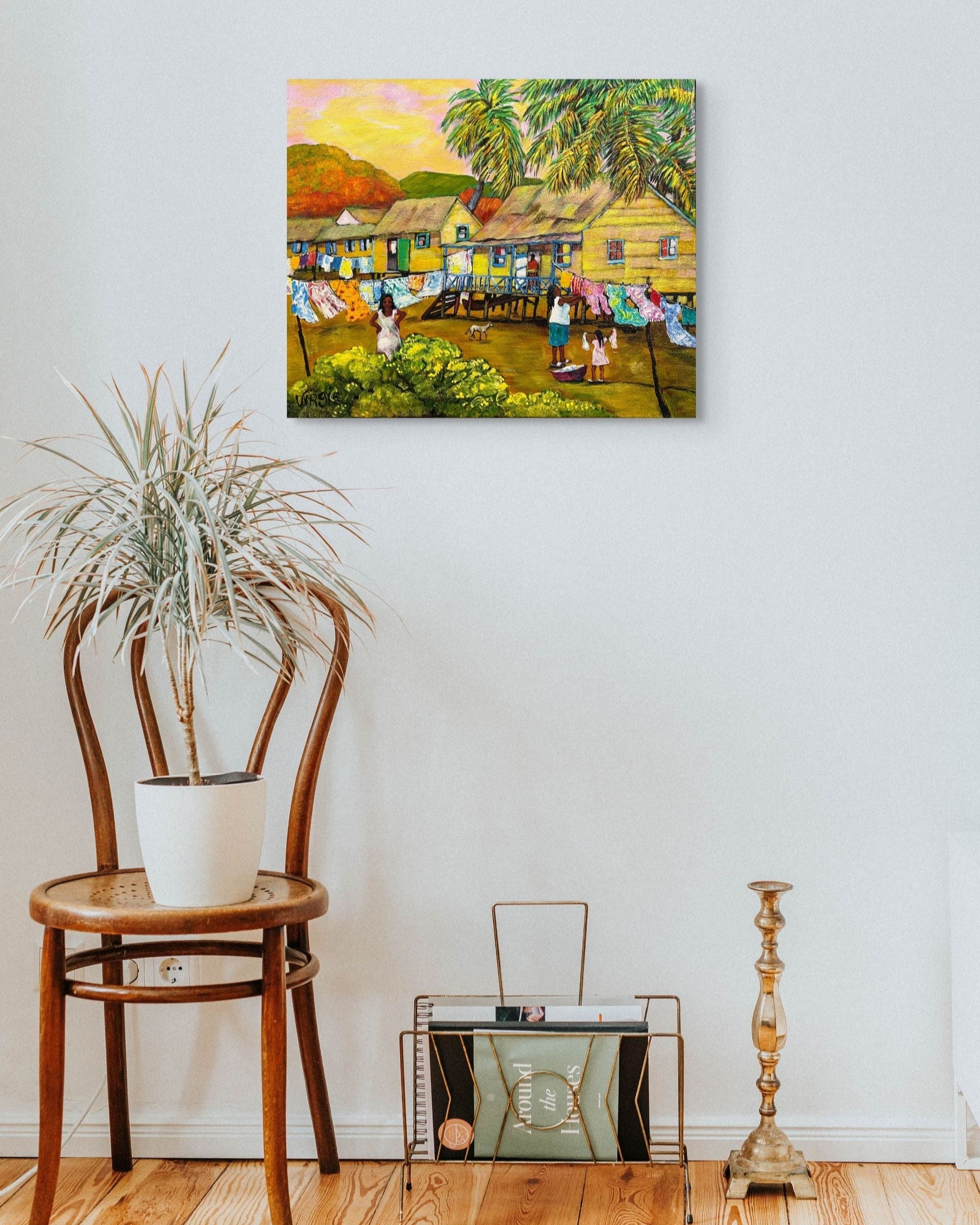 Painting of a village scene on a wall above a wooden chair with a plant and a small table.