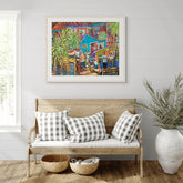 Colorful painting above a wooden bench with checkered pillows in a room with a plant and baskets.