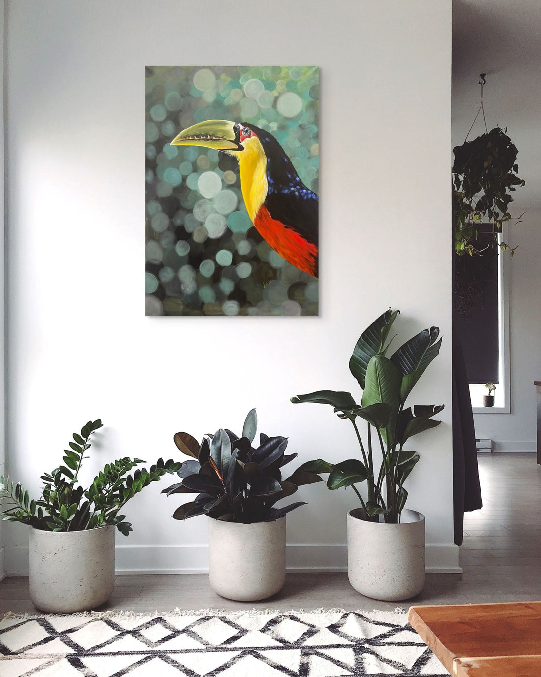 Room interior with potted plants and a colorful toucan painting on the wall.