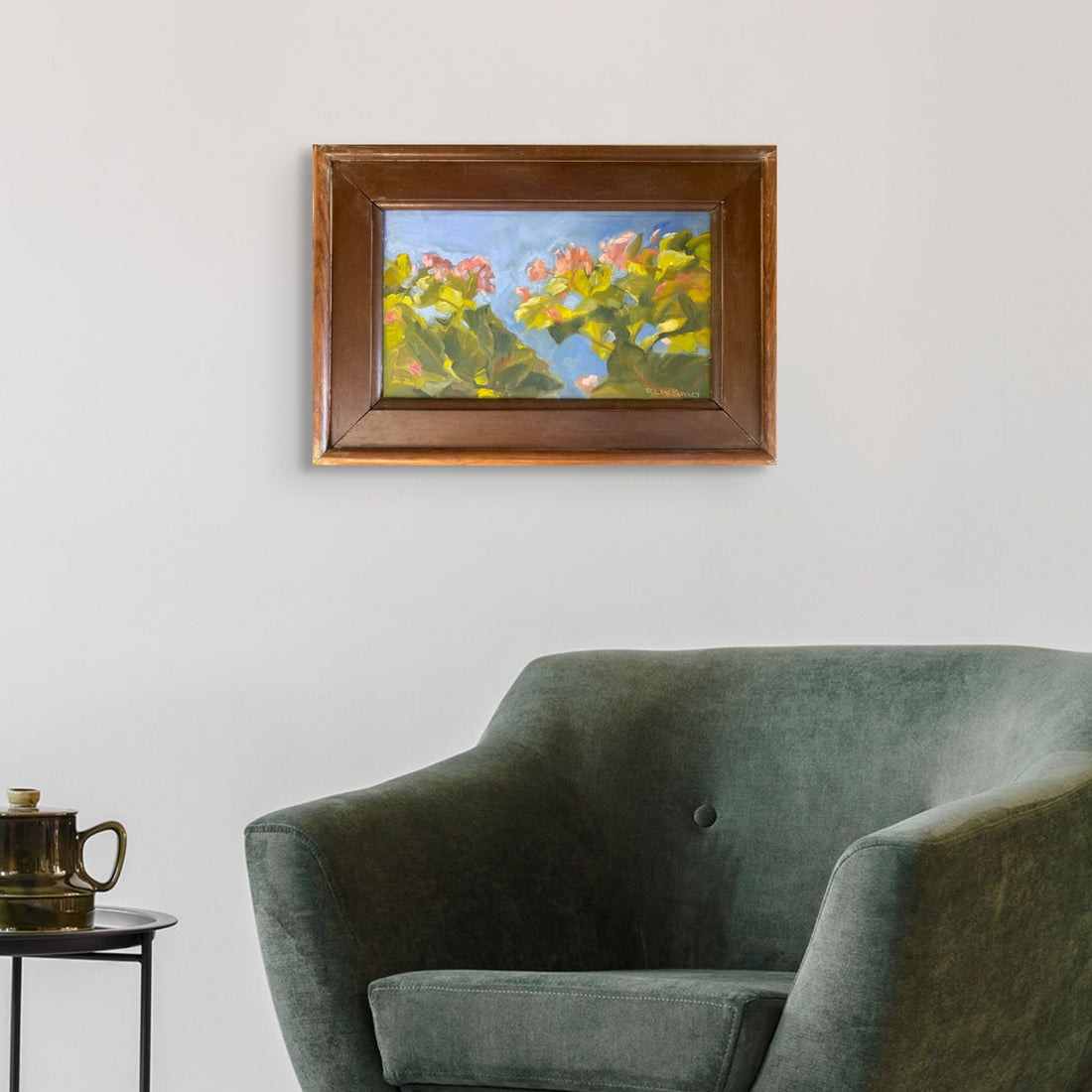 Framed painting of flowers on a wall above a green sofa.